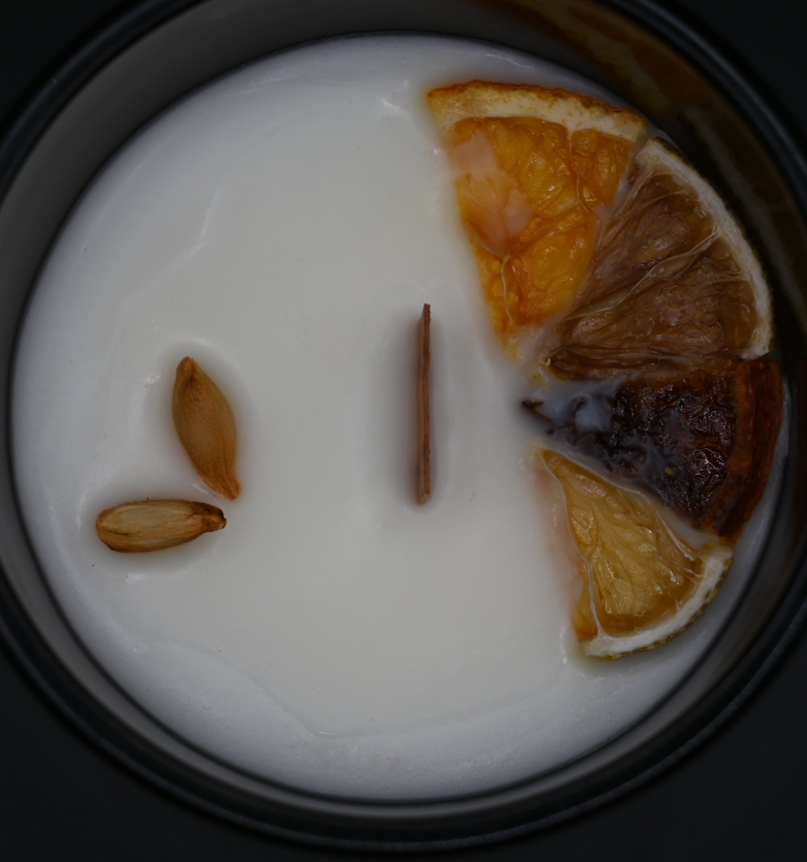 Candle with dried orange slices and seeds on a black background