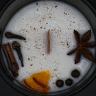 Spiced candle with star anise, cloves, and orange peel on a dark background