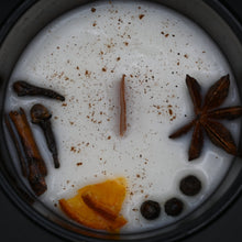 Spiced candle with star anise, cloves, and orange peel on a dark background