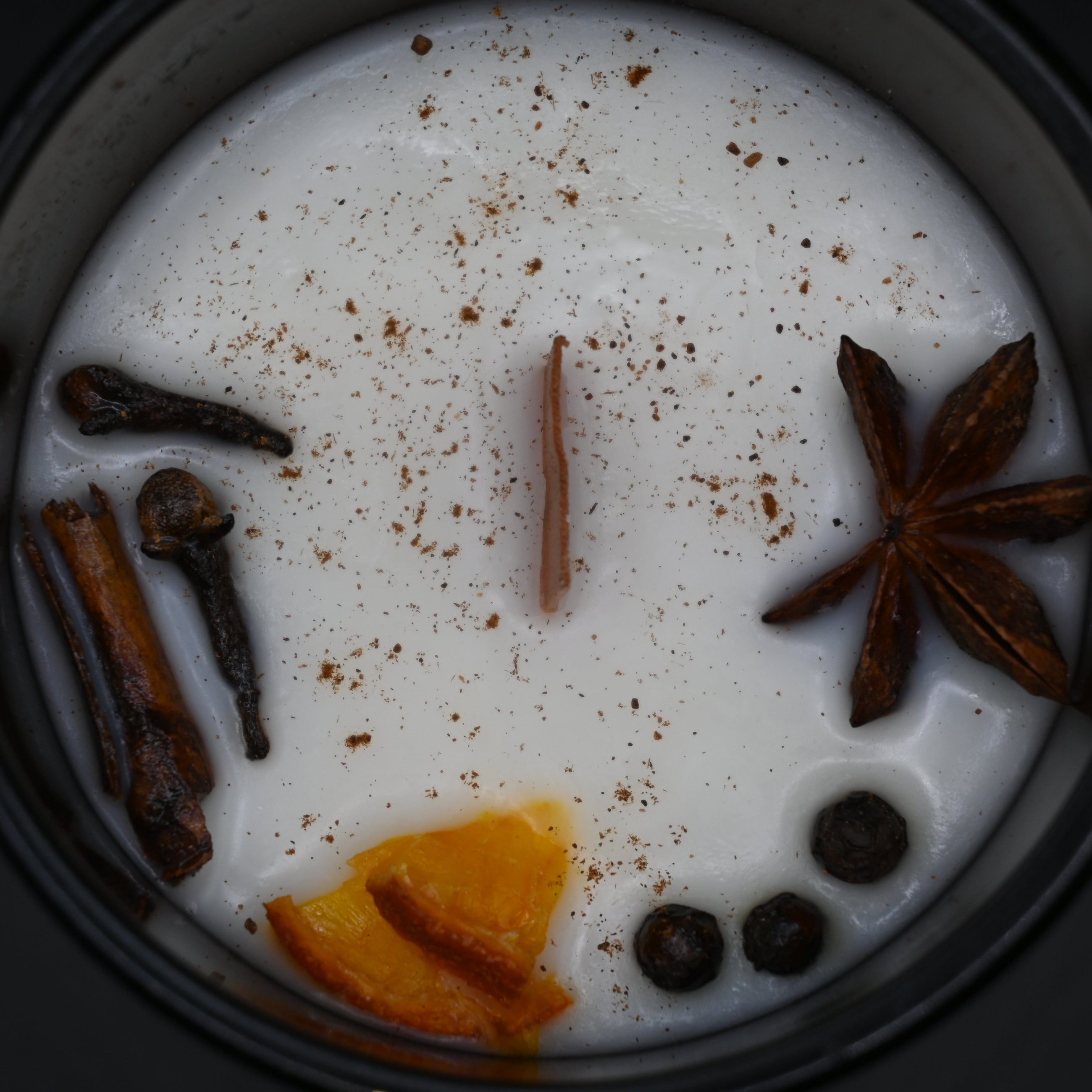Spiced candle with star anise, cloves, and orange peel on a dark background